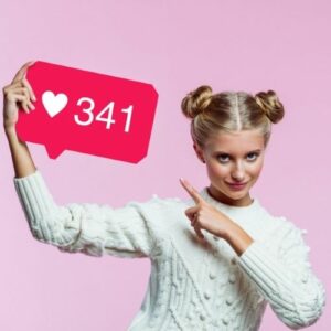 Photo of a blonde woman in a white sweater pointing to a sign with the TikTok heart icon and the number of likes.