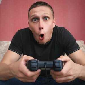 Close up photo of a main holding a gaming controller with an intense, surprised looked on his face. Make money online as a gaming streamer.