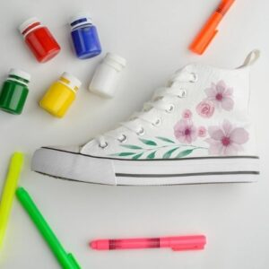 Photo of a white, high-top sneaker with hand-painted flowers on it, surrounded by markers and paint.