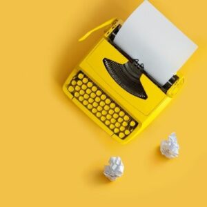 Photo of a yellow typewriter next to crumpled paper, against a yellow background. Start a blog to make money online.