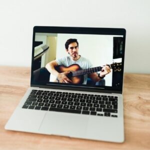 Close up photo of a laptop showing a video of man holding a guitar.